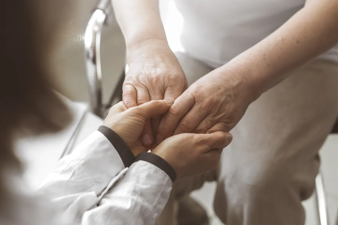 Professional sanitària agafant de les mans a una pacient